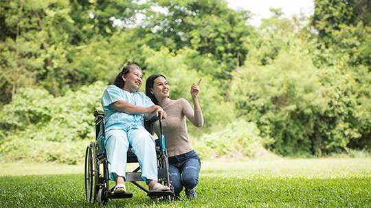 Two people, one in a wheelchairA family outdoors enjoying time together, representing temporary medium-term accommodation Melbourne , enjoying the outdoors and laughing together in a park for Disability Support Melbourne
