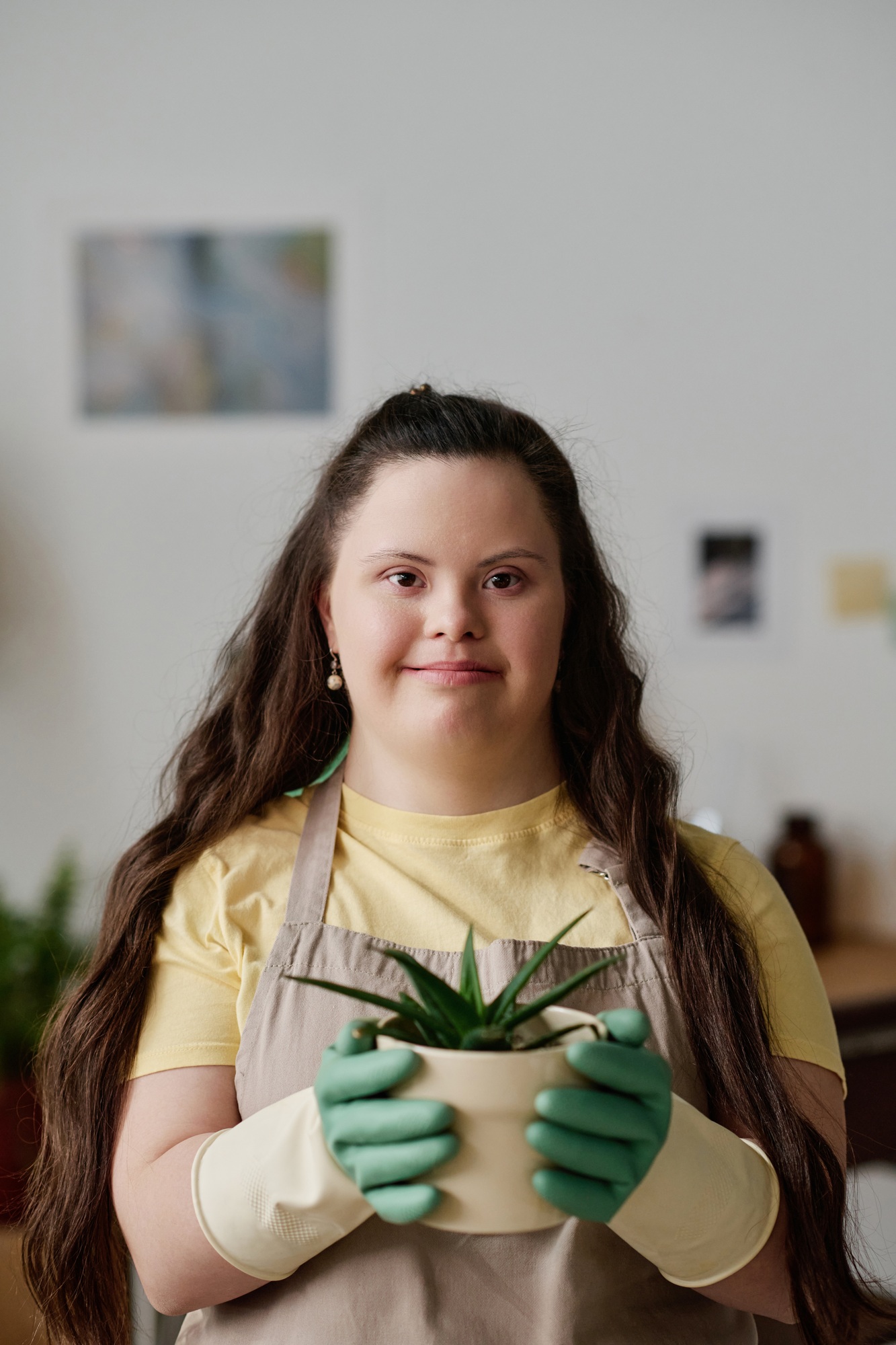 A young girl with Down syndrome happily holding a potted plant indoors for household task service melbourne