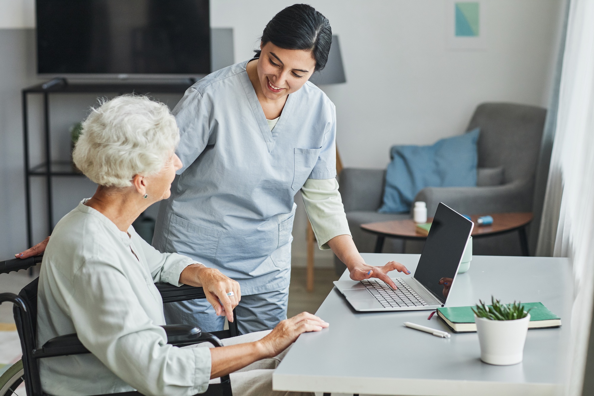 NDIS caregiver assisting an elderly woman using a laptop, guiding her through the ndis nursing care provider melbourne care plan process at home