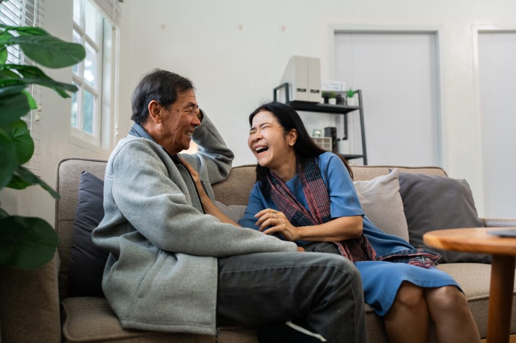 Elderly man and woman sitting on a couch, smiling and enjoying a conversation in a cosy home setting with household clean-up services in Melbourne.