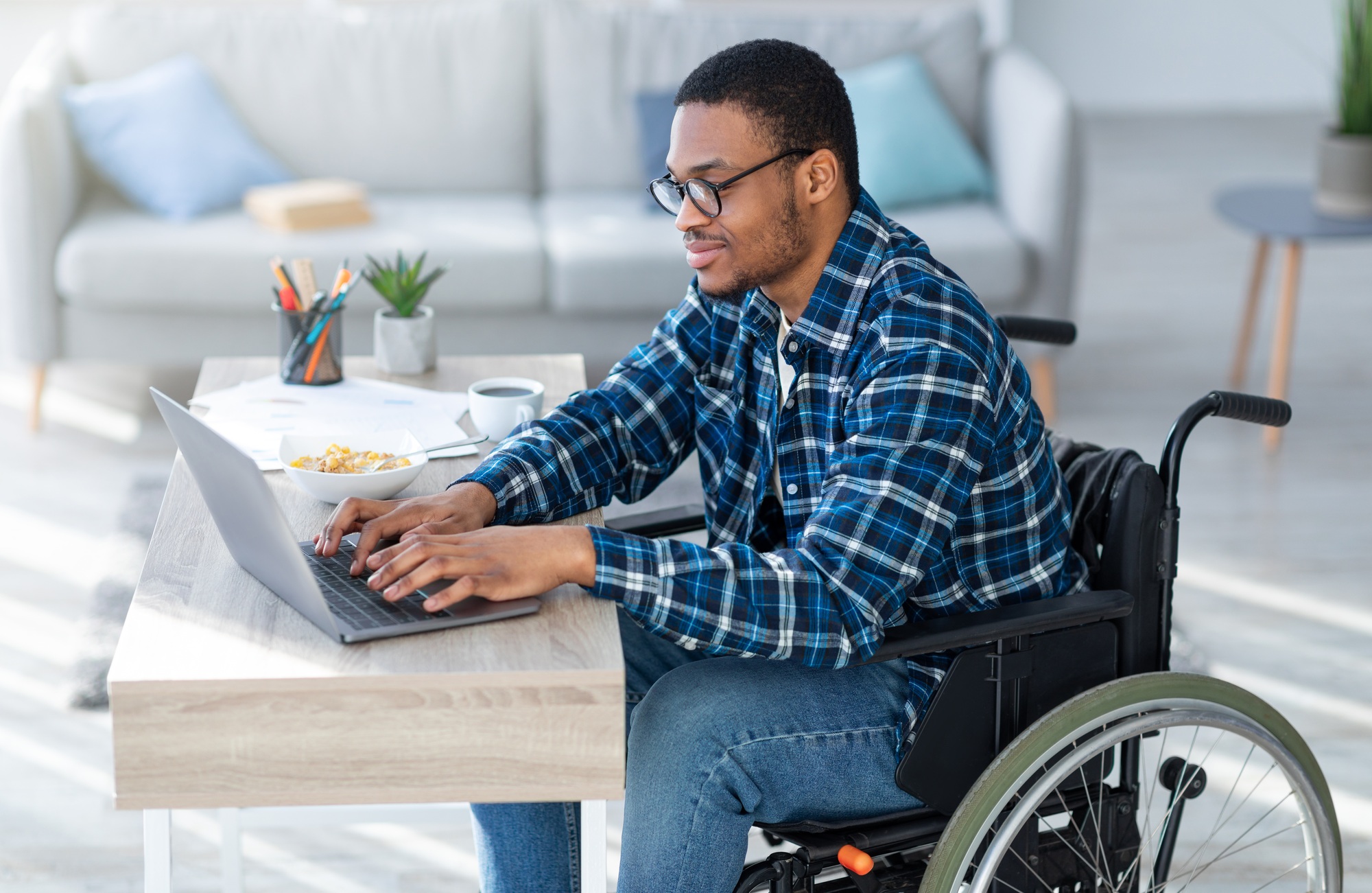 Man in a wheelchair using a laptop at home, representing accessible and empowering NDIS support coordination in Melbourne for individuals navigating their NDIS plans.